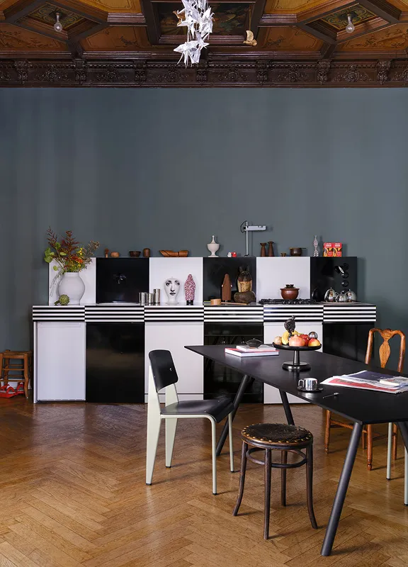 Essbereich im Altbau mit schwarzem Tisch, verschiedenen Stühlen und schwarz-weißem Sideboard vor blauer Wand
